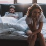 Smutna kobieta siedzi na brzegu łóżka, za nią mężczyzna w równie złym humorze, ponieważ odczuwa ból podczas stosunku
