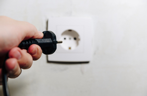 Ręka kierująca kabel do gniazdka przez porażeniem prądem