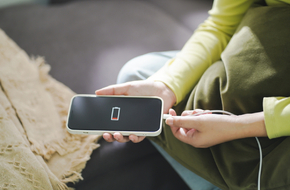 Młoda kobieta podłącza rozładowany smartfon do powerbanka.