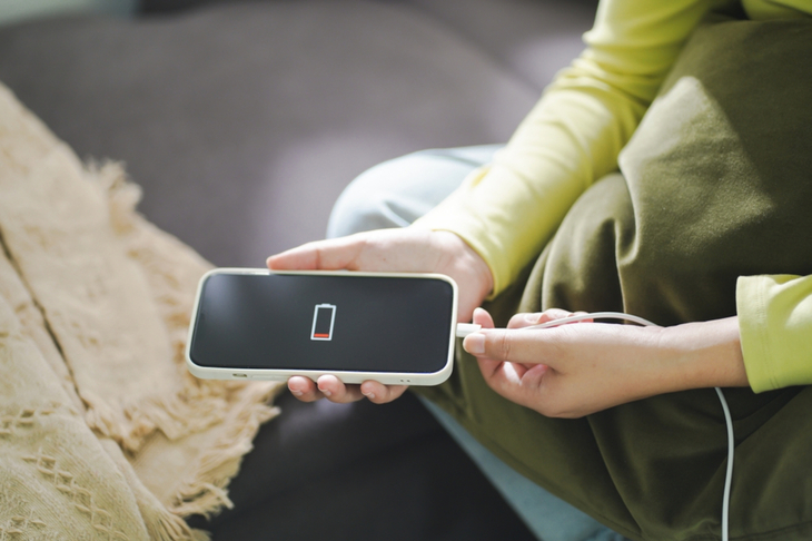 Młoda kobieta podłącza rozładowany smartfon do powerbanka.