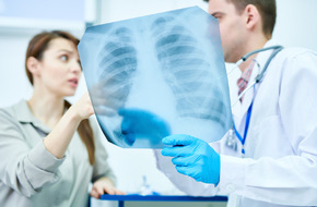 Zdjęcie przedstawia lekarza i pacjentkę omawiających rentgen klatki piersiowej, co może wskazywać na diagnostykę zapalenia opłucnej.