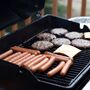 Grill z hamburgerami, kiełbaskami i plastrami sera grillującymi się na ruszcie. Ręka trzyma łopatkę do grillowania. Letni barbecue na zewnątrz.